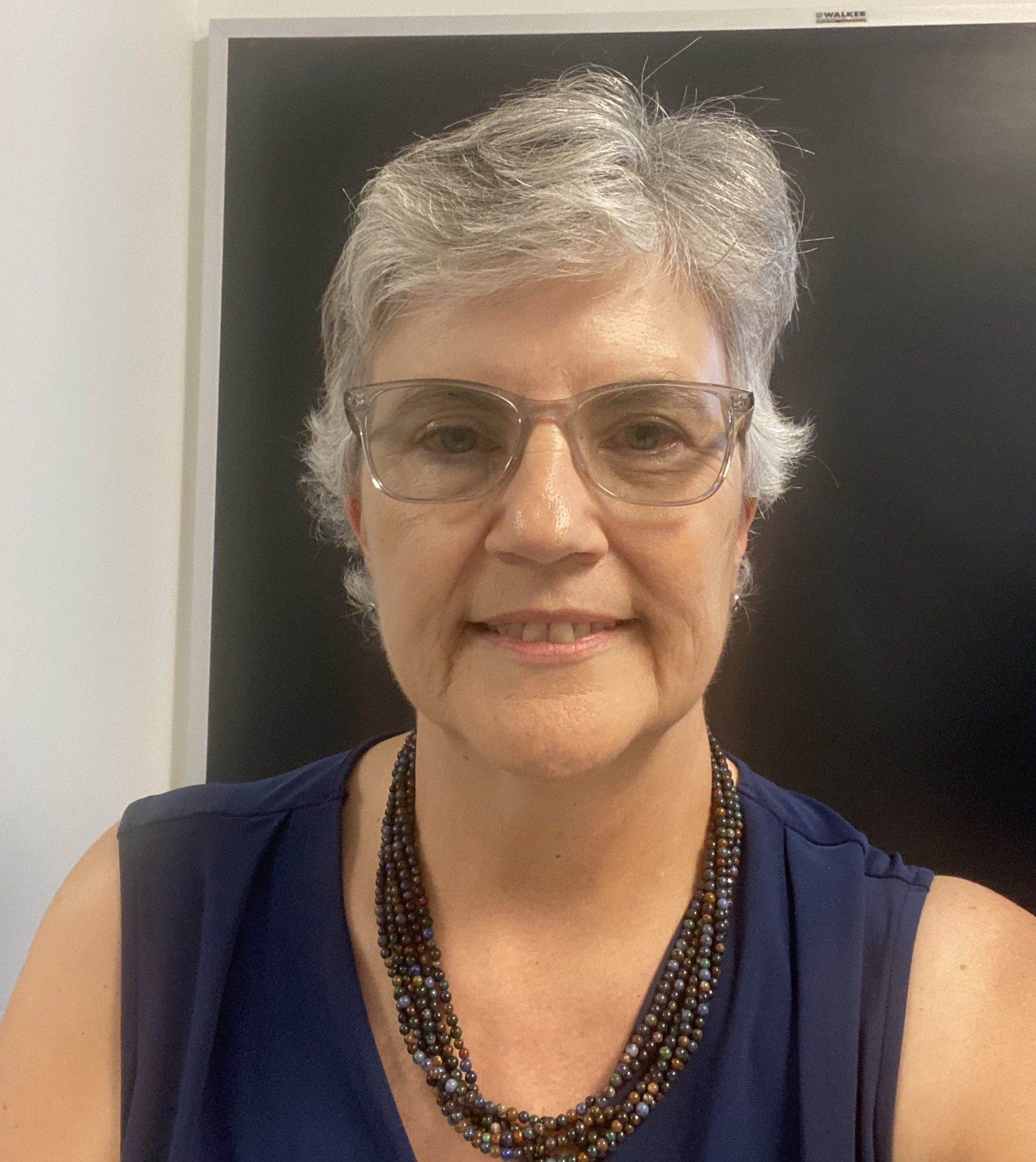 Woman with grey hair and glasses wearing a blue top